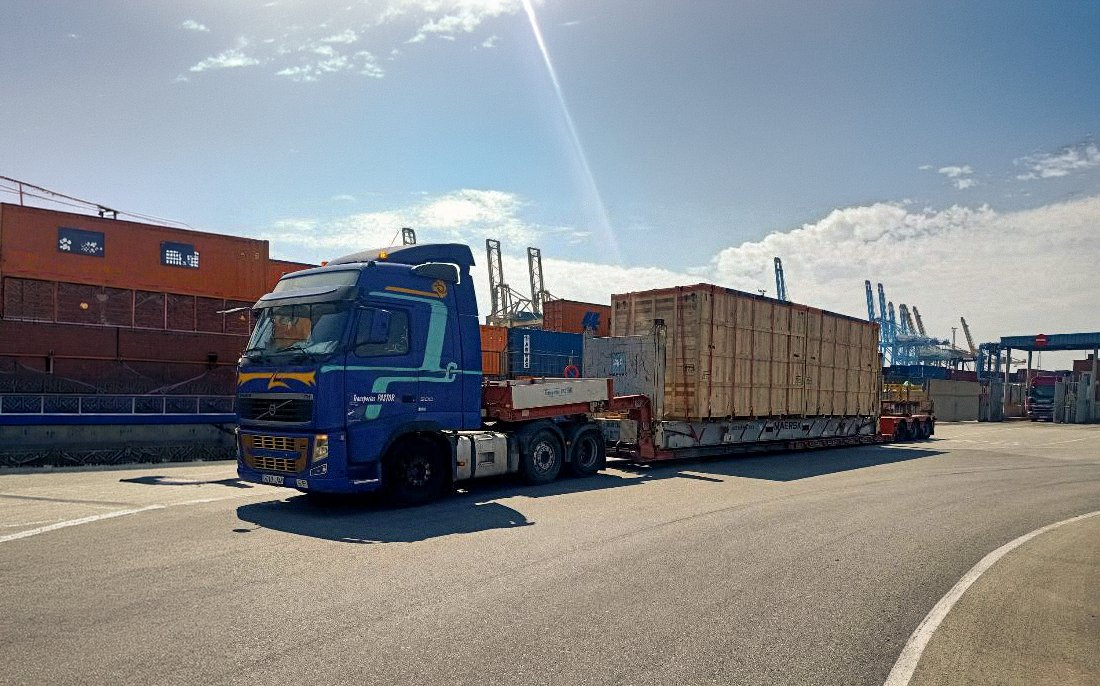 Tractora PASTOR con 45' flat rack cargado con un bulto embalado en madera, en terminal del Port de Barcelona.